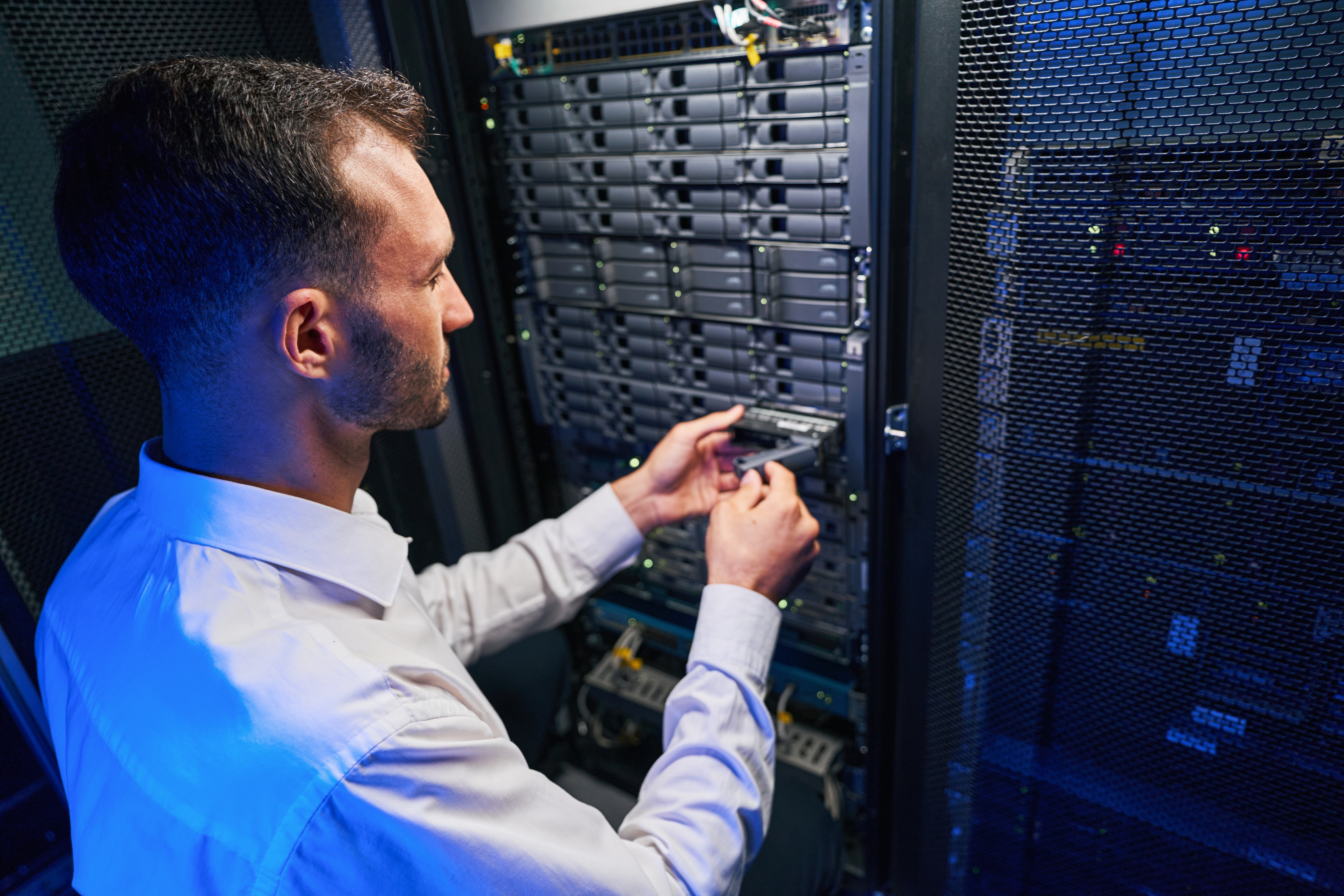IT professional inserting a hard drive into a server rack in a data center.