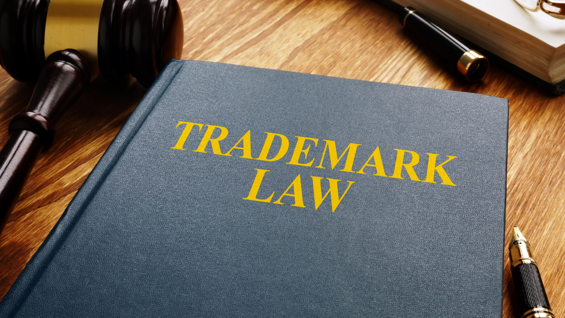 Close-up of a book titled “Trademark Law” on a wooden desk, with a gavel, fountain pen, and another book in the background, symbolizing legal and intellectual property concepts.