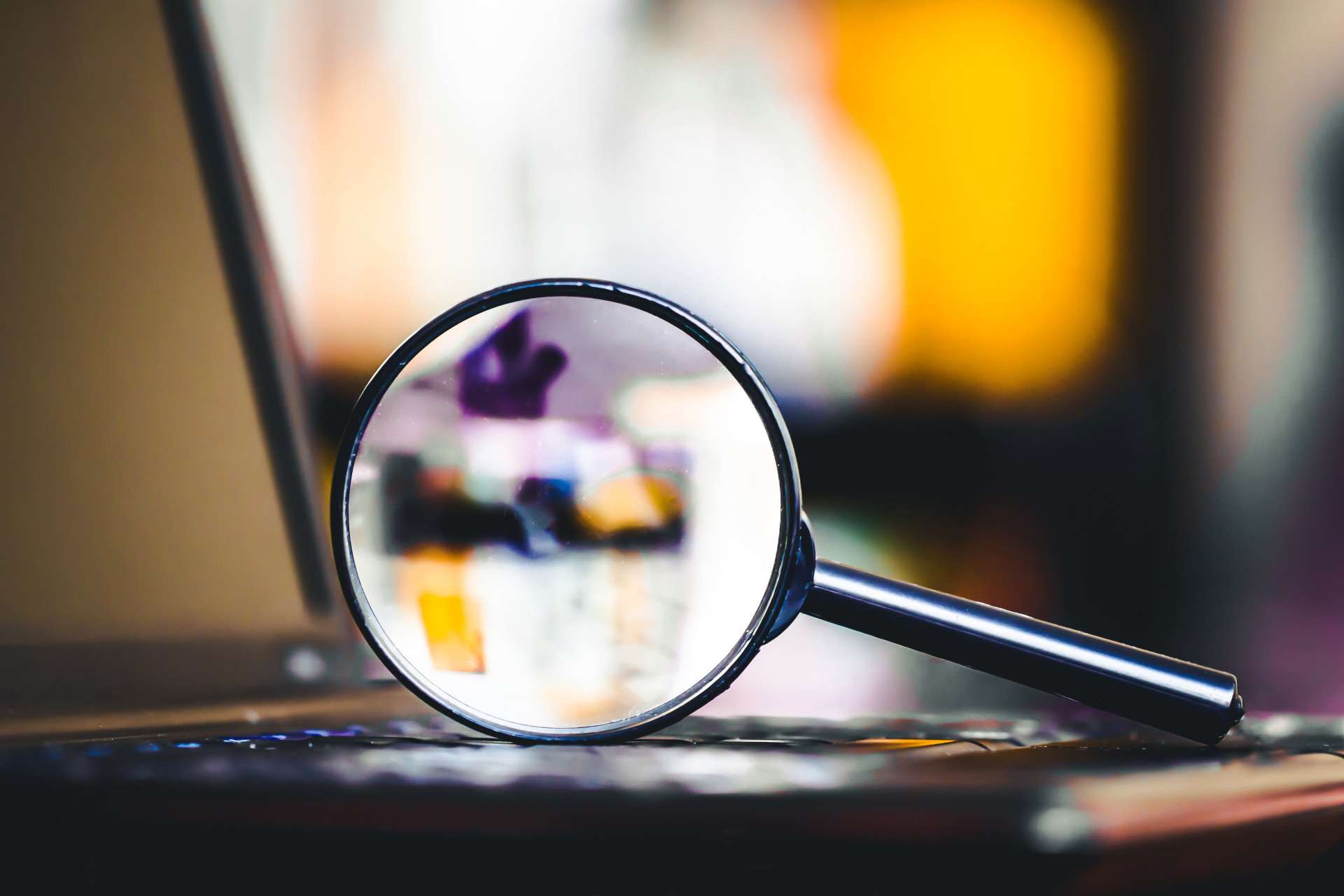  Magnifying glass resting on a laptop keyboard, symbolizing investigation, analysis, or digital forensics with a blurred background.