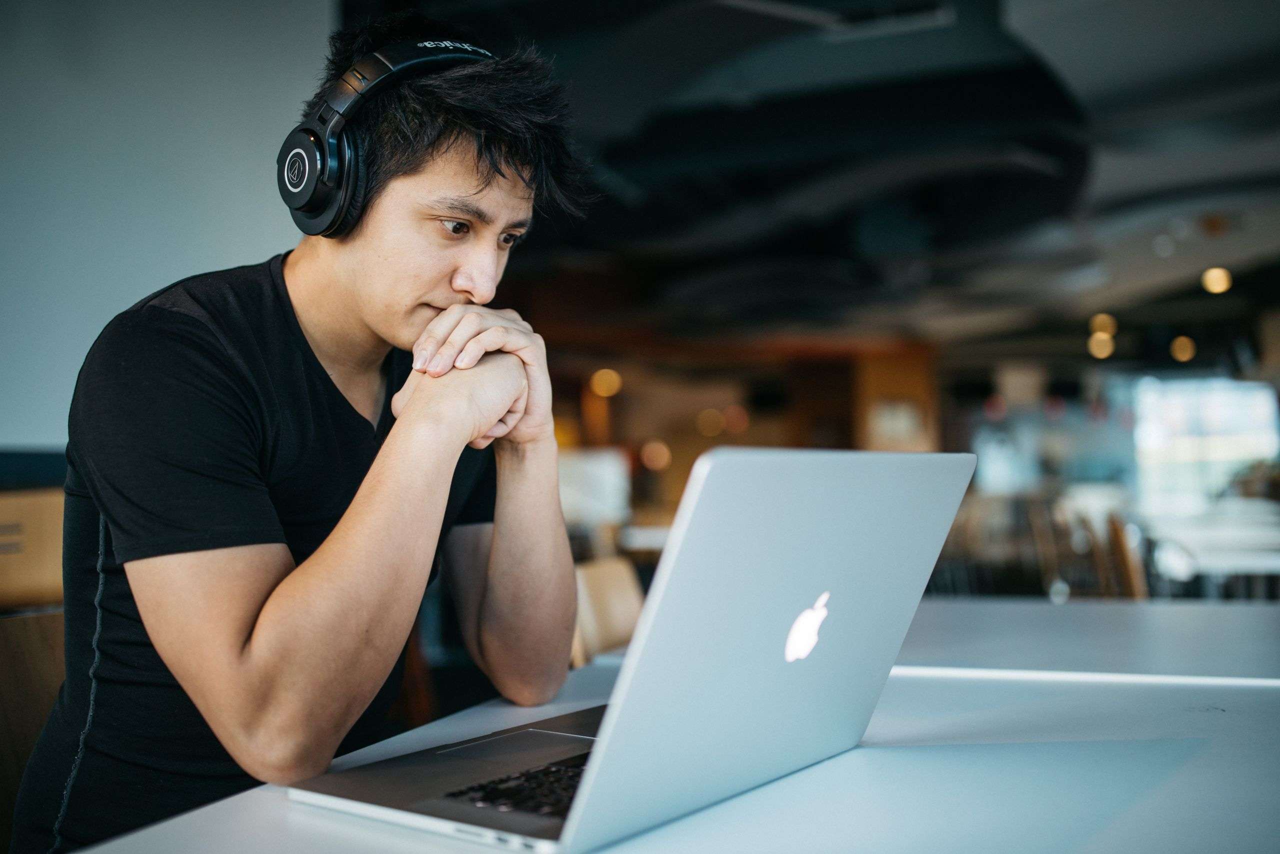 Person wearing headphones focused on a laptop screen, engaged in online learning in a modern workspace.